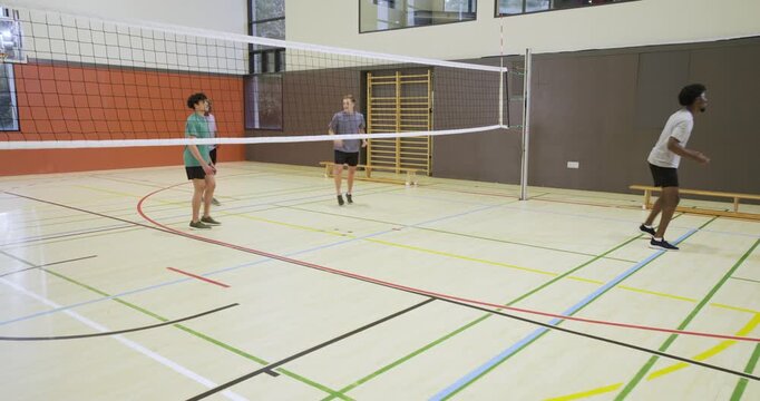 Diverse men receiving serve leaping at net huddling and celebrating point in gym wearing sportswear