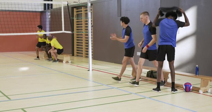 Blue team males clapping, walking onto court in gym starting rally with volleyball, copy space