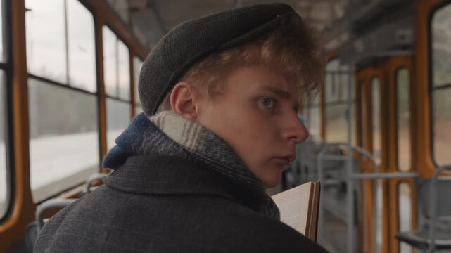 White filmmaker storyboarding during tram commute, young white man glancing sideways while marking notebook, vintage cabin and riverside panorama, contemplative atmosphere and planning of shots