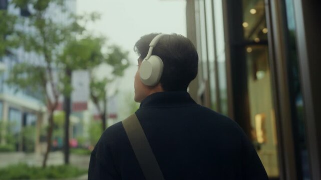 Young office worker in smart casual walks through the city with confidence , wireless headphones on, tuned into a self-growth podcast on productivity, emotional agility, and intentional career growth