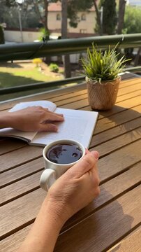 Vertical video happy Woman drinks cup of tea and reading book on sunny balcony. Cozy outdoor relaxation, slow living lifestyle, peaceful morning routine natural light, home comfort. Date with herself