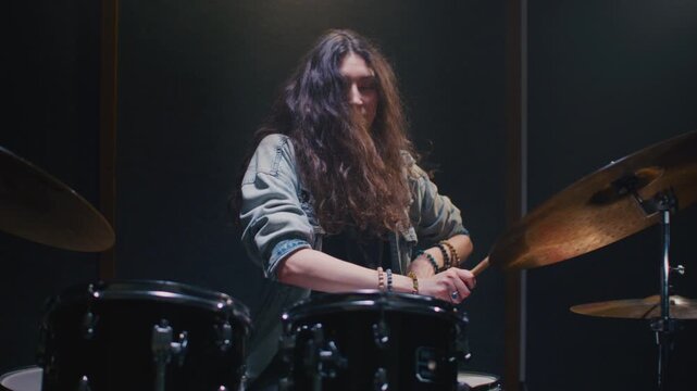 Woman drummer plays a drum kit, drumstick. Female musician beats a rock rhythm on drums, cymbals. Girl artist is rehearsing in a room or performing on festival stage. Alternative indie band in club