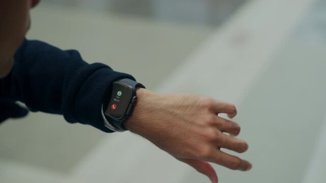 Young office worker walks through the city on his way to a meeting, taking a call on his smartwatch, blending wearable tech, mobility, and efficiency in modern fast-paced corporate routine