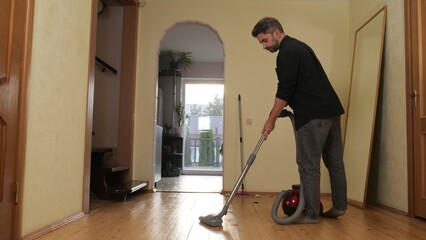 Fototapeta premium Man vacuuming wooden hallway floor in a modern apartment, focused on household chores and daily maintenance, demonstrating tidy, responsible domestic routine and floor care