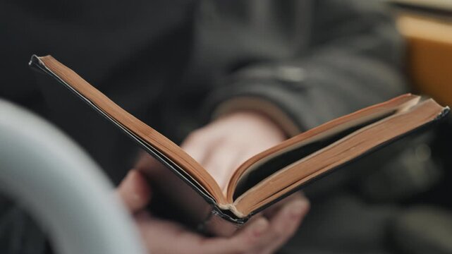 Open journal pages in hands, creator reviewing notes and turning sheets, tan page edges and stitched binding visible, closeup of fingertips and steady rhythm, purposeful commuter workspace vibe