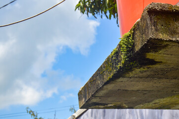 Concrete slab foundation for water tank with green moss. Aged cement structure against blue sky....