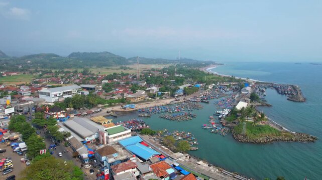 Aerial drone footage of the fishing local harbor in Pelabuhan Ratu, Sukabumi regency, Java island, Indonesia, with the big fish markets, hundreds of colorful wooden boats, with sea and houses behind