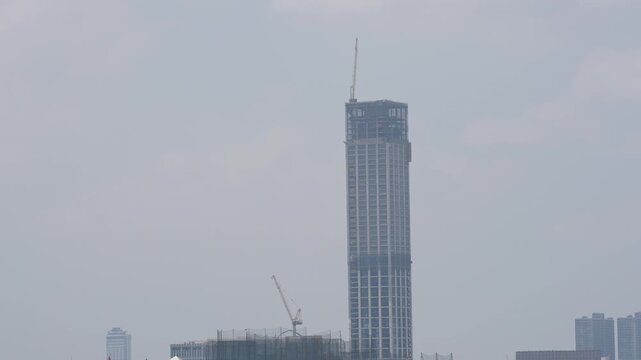 Skyscraper construction tower crane city skyline in urban haze, tall high rise building under foggy sky, modern city architecture development