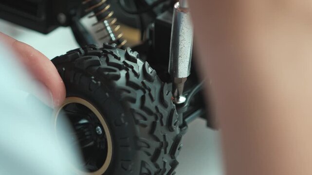 Close up of young student tighten the nut by using screwdriver. Caucasian teenager repairing or fixing car model while inspect robotic machine construction at STEM class. Focus on hand. Edification