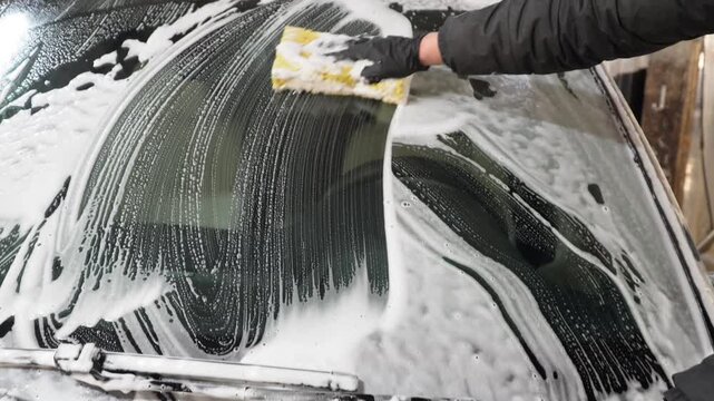 Car washer does full body car wash with soap and yellow sponge. Process of spraying foam on the auto body in the station. Second phase of detailing washing in car service. Cleaning the car.