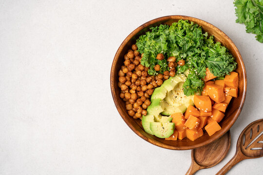 Vegan protein salad bowl with kale cabbage chickpeas roasted sweet potato and avocado in wooden bowl on light background, balanced plant based nutrition concept