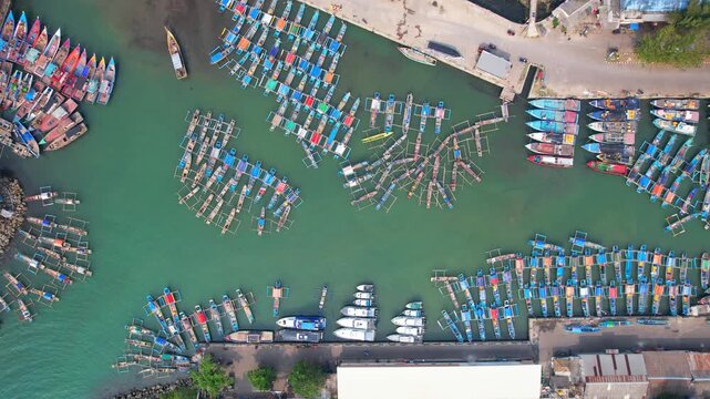 Aerial drone footage from above, of the fishing local harbor in Pelabuhan Ratu, Sukabumi regency, Java island, Indonesia, with hundreds of colorful local wooden boats, with jetty and turquoise water