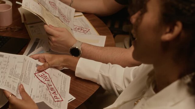 Over shoulder view of young couple holding household bills while sitting at round table in kitchen