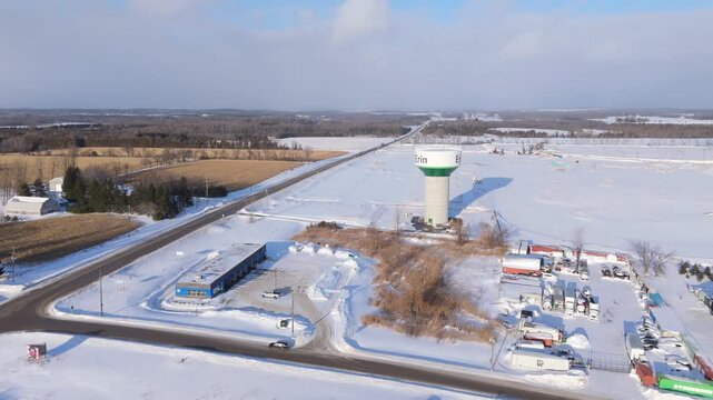Car Drives Past A Commercial Building With Water Tower In Winter Landscape At Erin, Ontario. Orbiting Aerial Shot.
