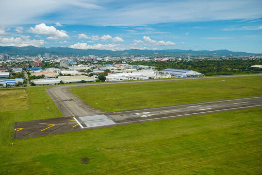Aerial view of a runway with a cityscape backdrop under a partly cloudy sky, Mactan, Philippines.