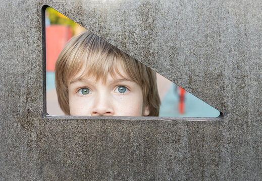 child peeks out from behind a triangle-shaped hole. A frightened look, eyes wide open. Hide and peek.