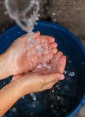 Fototapeta premium The water flows into the hands of the child. Selective focus.