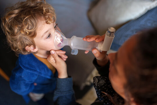Young child receiving respiratory medication with an inhaler and spacer mask for asthma treatment