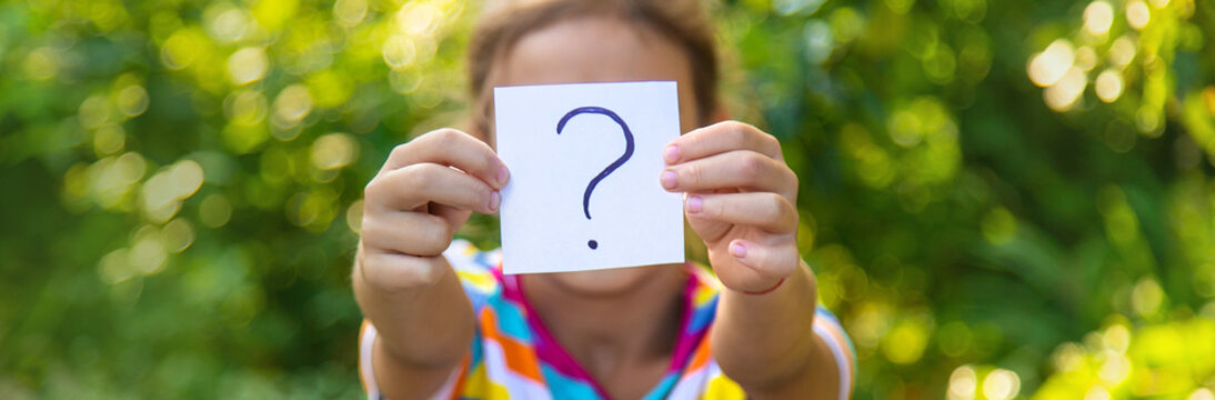 The child holds a paper with a question mark. Selective focus.