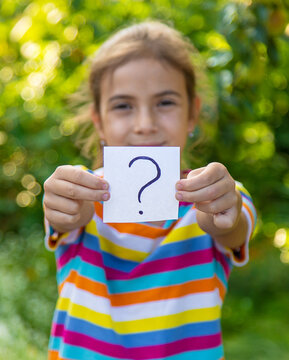 The child holds a paper with a question mark. Selective focus.