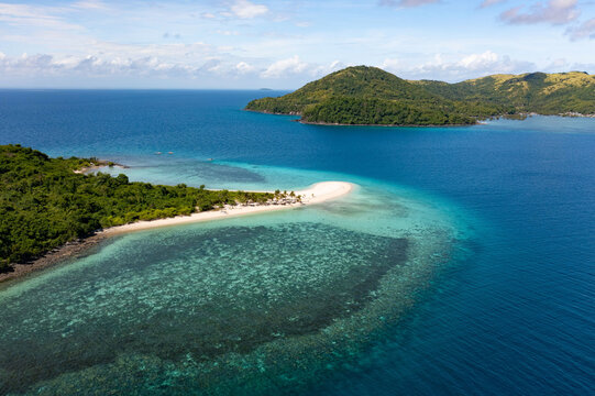 Aerial view of turquoise waters embracing a pristine sandbar, fringed by verdant trees under a vast sky, Concepcion, Western Visayas, Philippines.