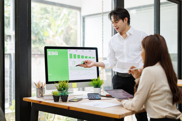 Obraz premium Asian Business Colleagues Discussing ESG Metrics on Desktop Monitor