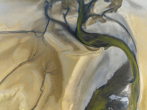 Aerial view of a river snaking through the landscape, cutting through the sand with green and brown tones, creating a striking contrast of colours, Walvis Bay, Erongo Region, Namibia.