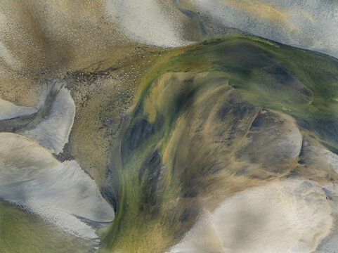 Aerial view of swirling patterns of sand and water create mesmerizing abstract art, with colors ranging from pale beige to deep green, Walvis Bay, Namibia.
