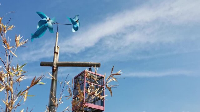 Decorative pole with blue pinwheels and cage under clear sky