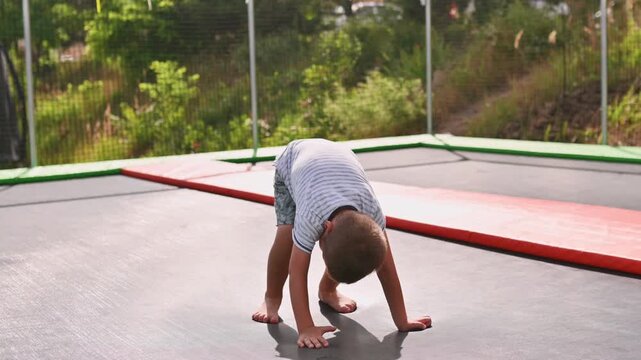 A preschooler jumps on a trampoline in a park during the summer. Safe children's activities under parental supervision. Safety precautions for jumping on a trampoline with a net.