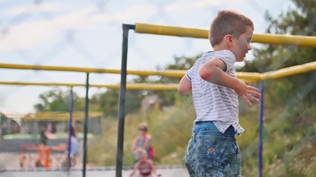 A preschooler jumps on a trampoline in a park during the summer. Safe children's activities under parental supervision. Safety precautions for jumping on a trampoline with a net.