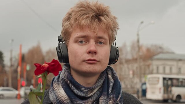 White creator listening with closed eyes in headphones, songwriter mood by urban bus stop with rose at side, meditative scarfed artist in autumn light, calm reflective street portrait and subtle