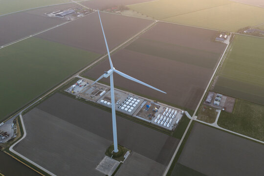 Aerial view of wind turbine generating clean energy, with a large scale battery storage system in a rural landscape, symbolizing sustainable power