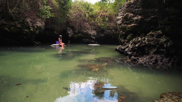 Woman swimming alongside rescued green sea turtles in the natural tidal pool of Baraka Natural Aquarium. High-angle view showcasing gentle marine life interaction in Zanzibar