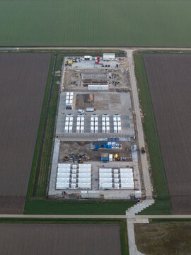 Aerial view of a large battery energy storage system under construction, showing modular units and green fields