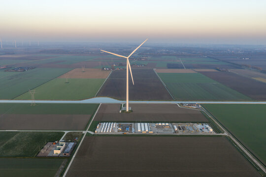 Aerial view of wind turbine generating clean energy, connected to a battery storage system in a rural field landscape, promoting sustainability