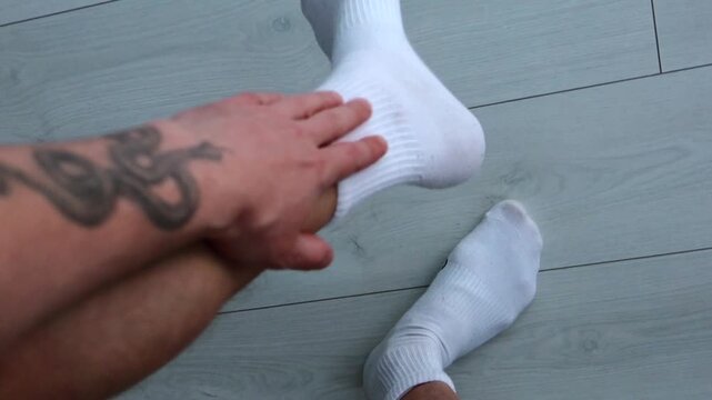 An itchy leg on a man in white socks.
A man stands on a white wooden floor and scratches his legs.