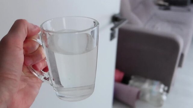 A man walks around the room in white socks with a cup of drinking water