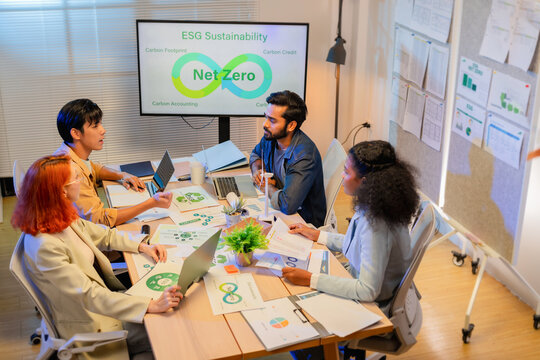 Diverse multiracial business team discussing ESG sustainability net zero strategy around table with wind turbine model and screen in modern office, ideal for green corporate concepts.