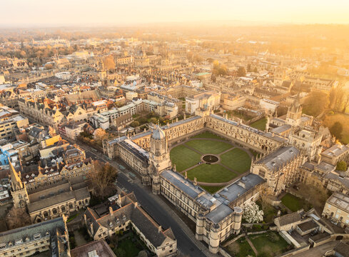 Aerial view of golden light kissing the honeyed stones of Oxford's historic buildings, revealing the intricate architecture of Christ Church College, Oxford, England, United Kingdom.