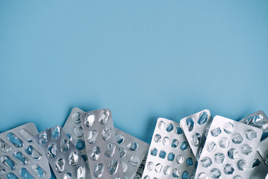 Empty silver blister packs form border at bottom of blue background. Non-recyclable medical waste, plastic pollution in healthcare, eco-friendly pharmacy.