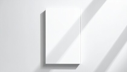 Obraz premium Blank white book cover mockup on a wall with realistic window shadow overlay for design presentation.