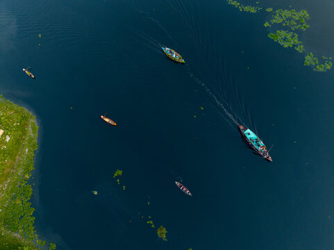 Aerial view of boats cutting through the dark waters, leaving white wakes, amidst patches of green vegetation, Dhaka, Dhaka Division, Bangladesh.