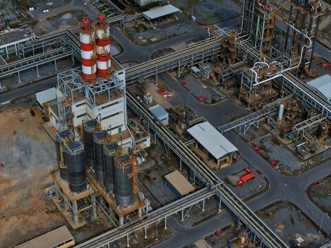 Aerial view of a sprawling industrial complex with towering smokestacks and a network of pipes, contrasting against the geometric precision of roads, Thessaloniki, Greece