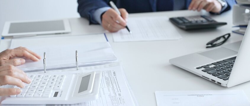 Close up of female accountant hands using calculator while collaborating with male colleague in office, calculating taxes and analyzing financial data. Audit and taxes in business