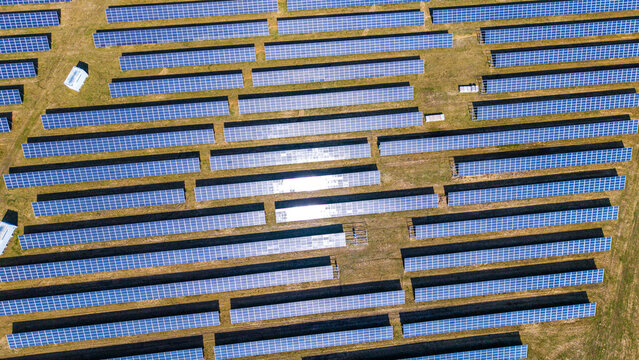 Aerial view of expansive solar arrays basking under the sun, juxtaposed against the golden fields, creating a stark contrast of technology and nature, Sevetin, South Bohemian Region, Czechia.