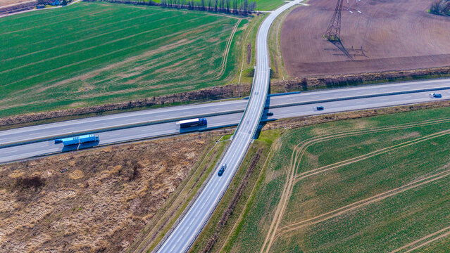 Aerial view of a highway intersected by a bridge, flanked by agricultural fields with contrasting colors, textures, and tones, Sevetin, South Bohemian Region, Czechia.
