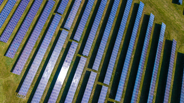 Aerial view of rows of solar panels shimmering under the sun, nestled in the green fields of Sevetin Solar fields, Sevetin, South Bohemian Region, Czechia.