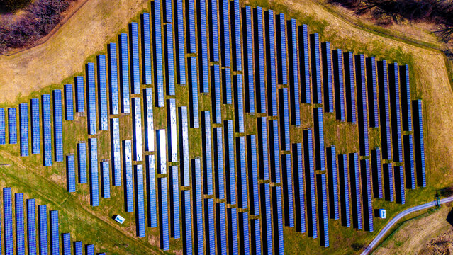 Aerial view of symmetrical solar panels casting a blue sheen across the verdant fields, juxtaposed against the golden hues of late autumn, Sevetin, South Bohemian Region, Czechia.