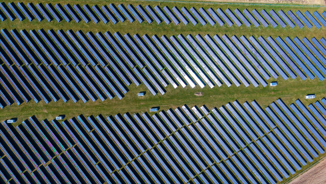 Aerial view of solar panels arrayed in neat rows, glinting under the sun's glare amidst the green fields, Sevetin, South Bohemian Region, Czechia.